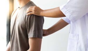 A person in comfortable clothing receiving a gentle spinal adjustment from a professional in a clinical setting.