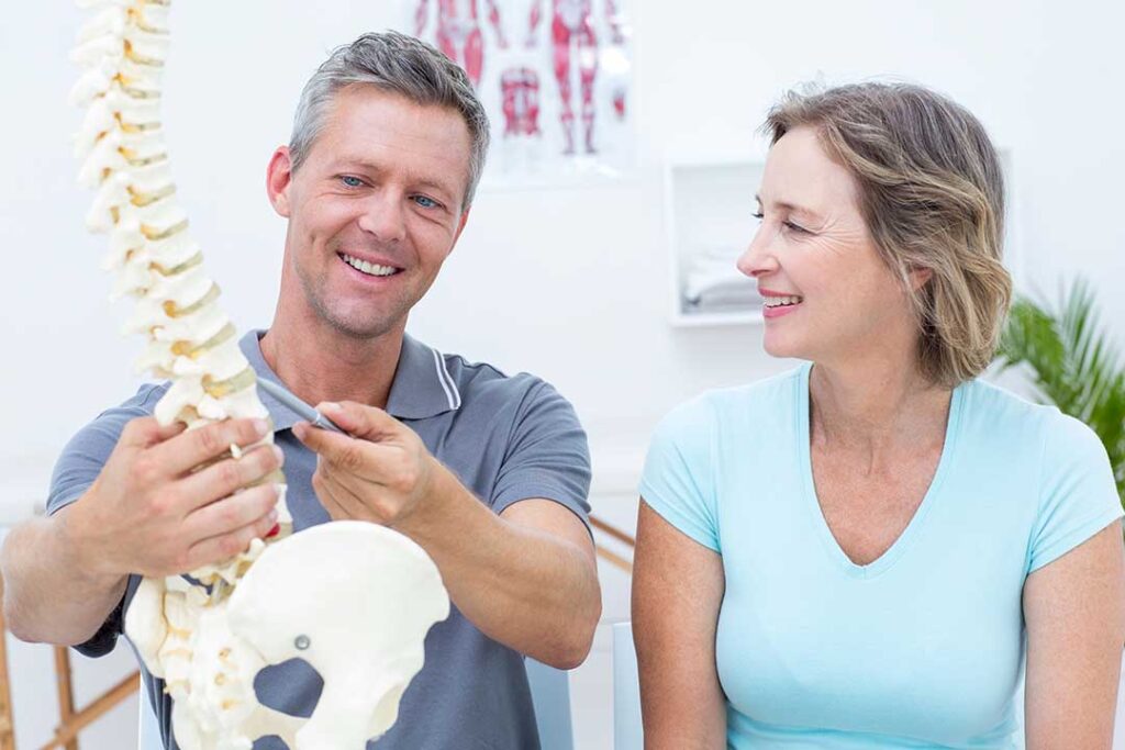 Person performing a balance exercise beside a support rail while a clinician observes neck and posture alignment.