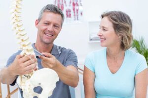 Person performing a balance exercise beside a support rail while a clinician observes neck and posture alignment.